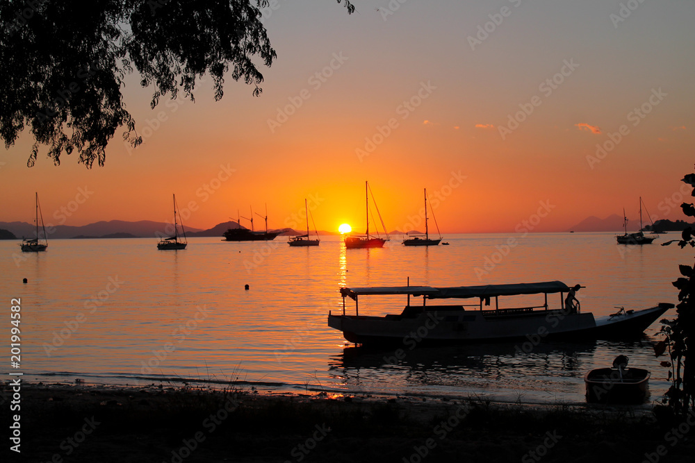 beautiful tropical sunset by the beach with silhouette of boats.