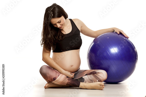 a young beautiful pregnant woman posing with a fitness ball on a white background