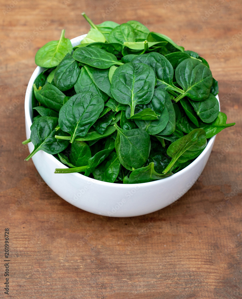 Fresh baby spinach in a bowl on rustic wooden background, top view. Copy space. Fresh baby spinach in a bowl on rustic wooden background, top view. Copy space.