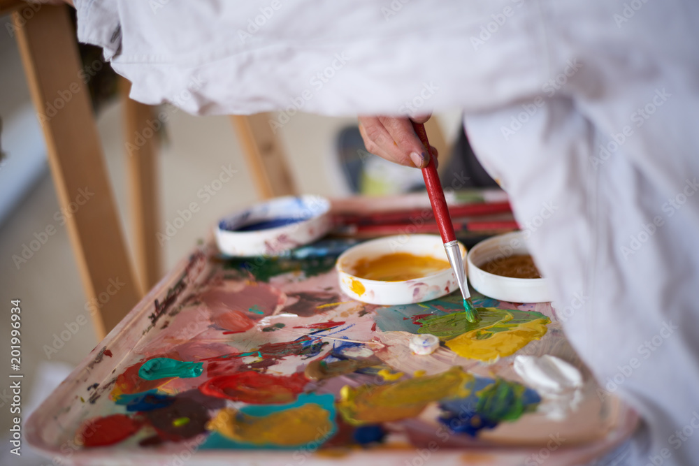 Close up of girl`s hands holding paint brush and mixing colors for painting. Close up of girl`s hands holding paint brush and mixing colors for painting.
