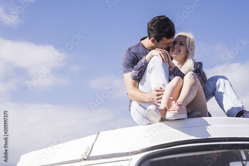 caucasian nice group of people man and woman hug together on the top of a vintage van. vacation time and leisure activity outdoor with blue sky in background. sunny day and nice weather warm