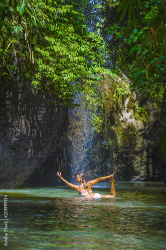 attractive and fit tourist Caucasian woman practicing yoga exercise pose in amazing tropical exotic waterfall lagoon with green turquoise water color © TheVisualsYouNeed