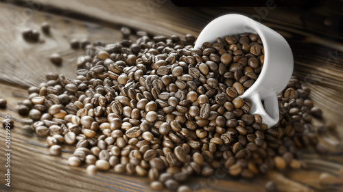 Coffee beans are poured from a Cup on a wooden background. Copy space for text. Dark background.