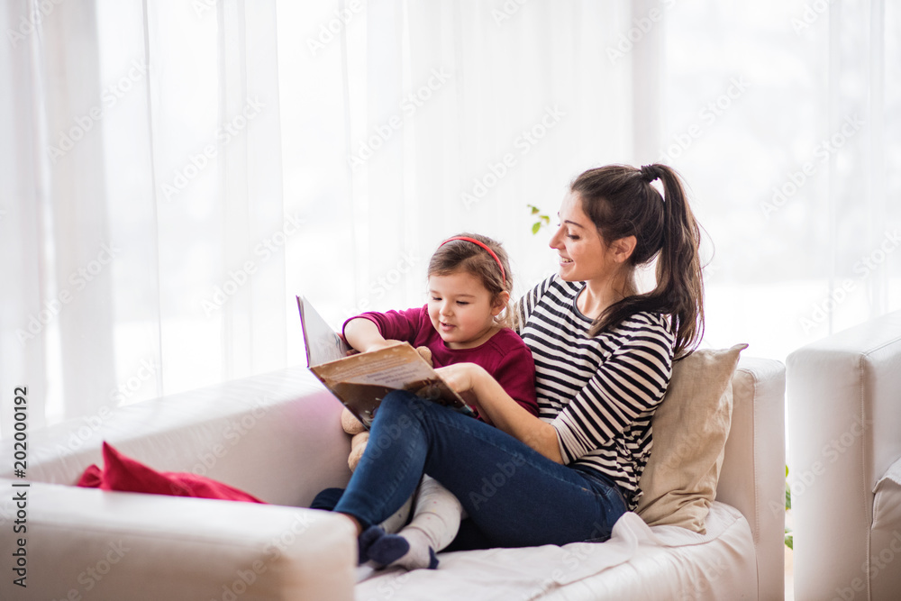 Young mother with a small girl at home, reading a book.