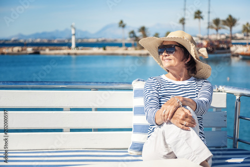 beautiful stylish elderly woman travels on a yacht, on a background of a resort and the sea. Active pensioners, vacations, travel