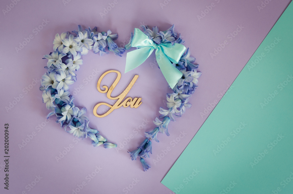 Heart made from hyacinths blossoms and mint bow on purple background with wooden letters You. Floral flat lay minimalism patterns greeting card. Top view, place for text. Heart made from hyacinths blossoms and mint bow on purple background with wooden letters You. Floral flat lay minimalism patterns greeting card. Top view, place for text.