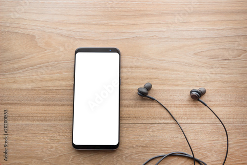 Technology concept, smartphone with white screen and black headphone cable on wood table background,top view.