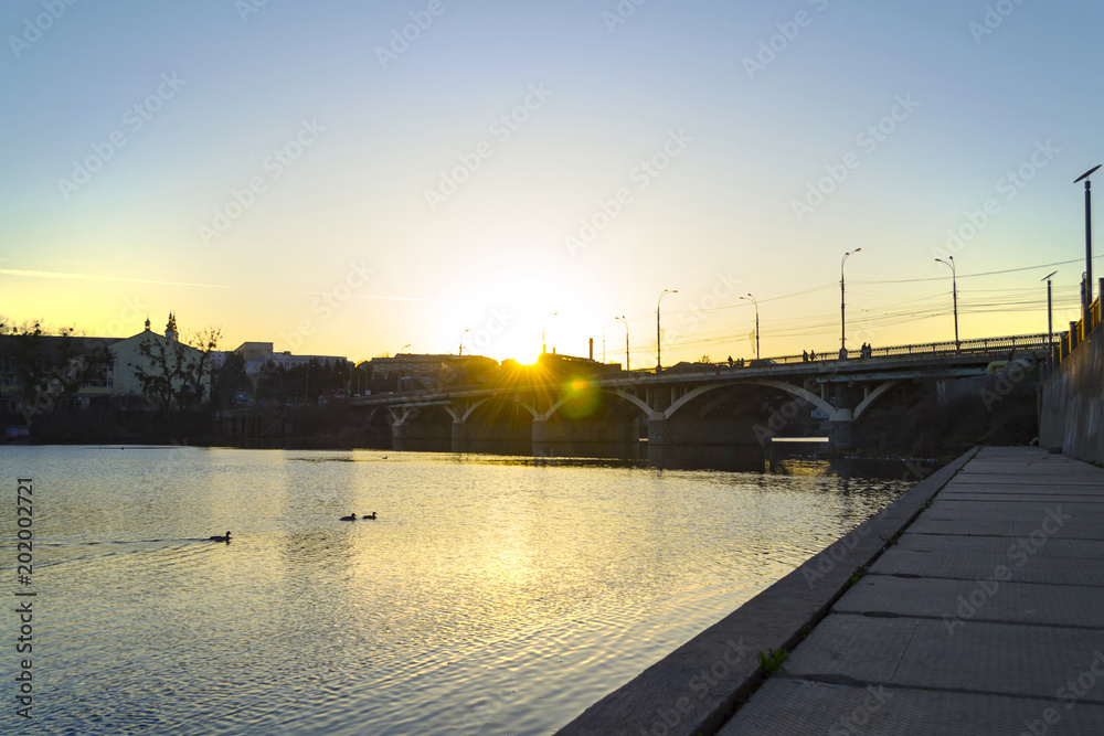 Fantastic colorful sunset in city on river with reflections and lens flare