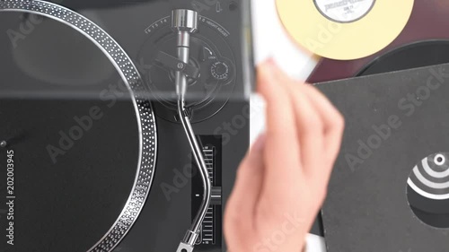 Slide the side view to the hands of the DJ's girl put a black vinyl record on the  rotating disc of the turntable and the needle the stylus, black headphone