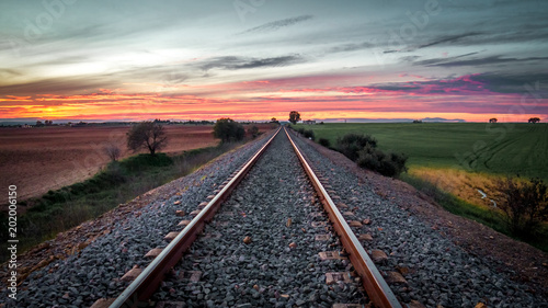 train tracks in the middle of the field with red sunset background