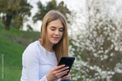 Young beautiful woman with long blond hair sits with a tablet in a blooming garden