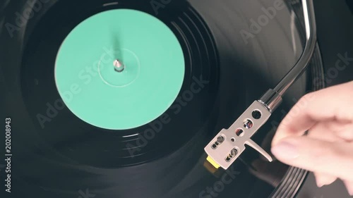 The vinyl record on DJ turntable record player close up. Black vinyl background with a green screen in the center. The girl's hand puts the stylus with the needle on a rotating black vinyl record