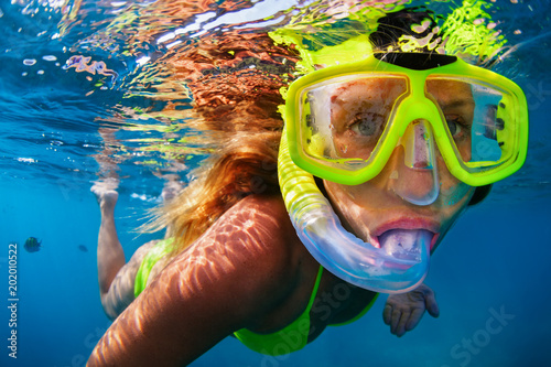 Happy girl in snorkeling mask dive underwater with tropical fishes in coral reef sea pool. Travel lifestyle, water sports, outdoor adventure, swimming lessons on family summer beach holiday with kids