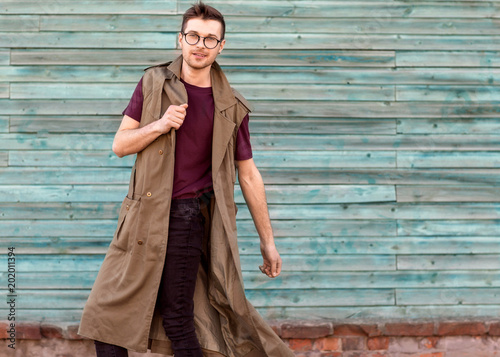 fashion guy in glasses poses near a wooden wall in blue.