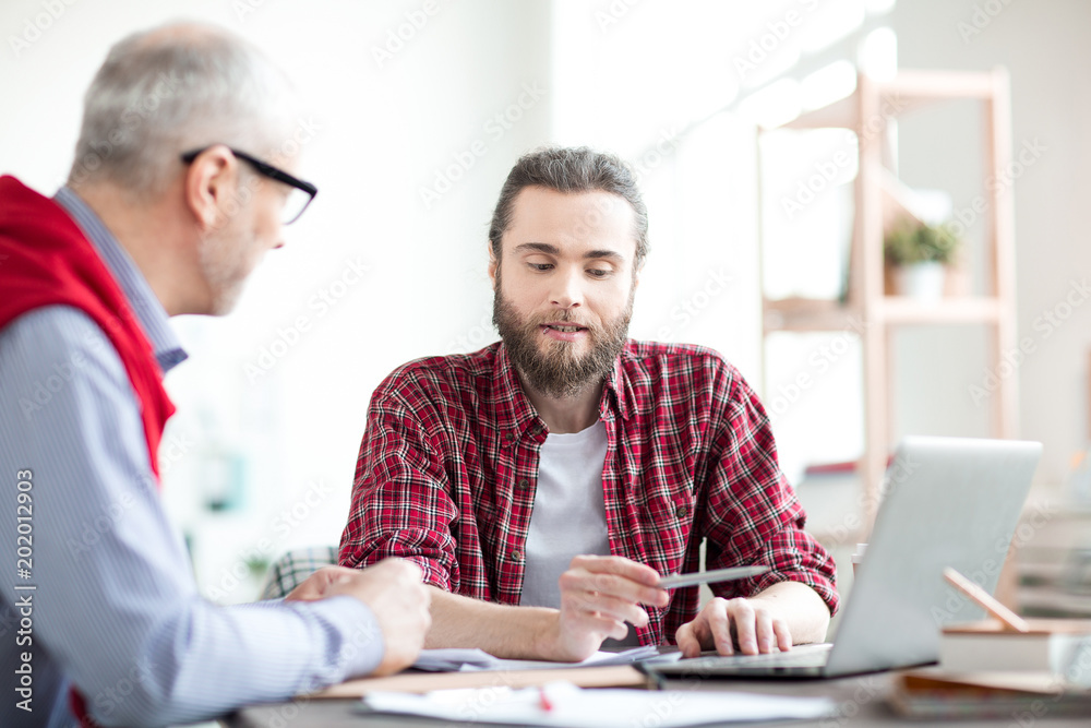 Young manager pointing at laptop and discussing business presentation with his coworker Young manager pointing at laptop and discussing business presentation with his coworker