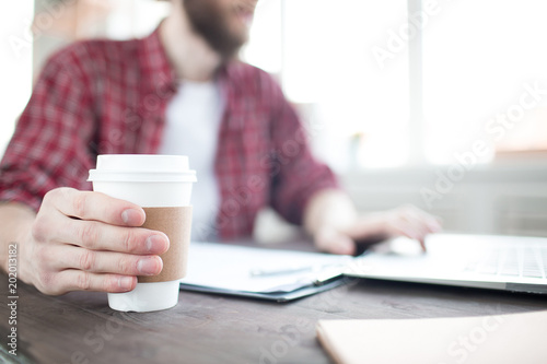 Close-up of coffee cup in male hands. Man sitting at the table and working and drinking coffee