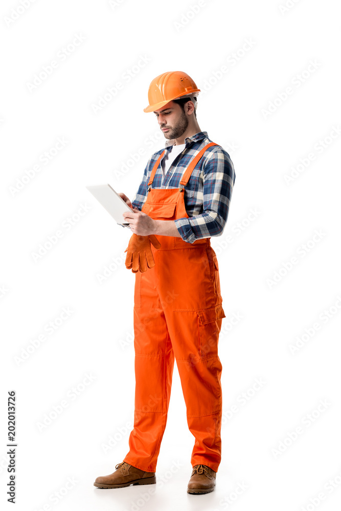 Young repairman in orange overall and hard hat using digital tablet isolated on white Young repairman in orange overall and hard hat using digital tablet isolated on white