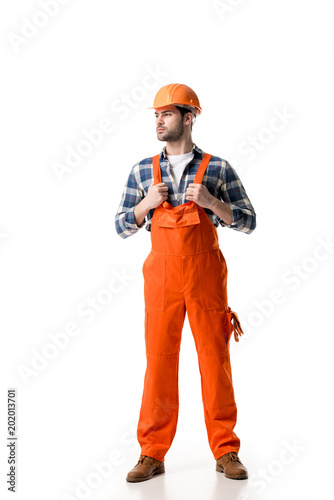 Confident handyman in orange overall and helmet isolated on white