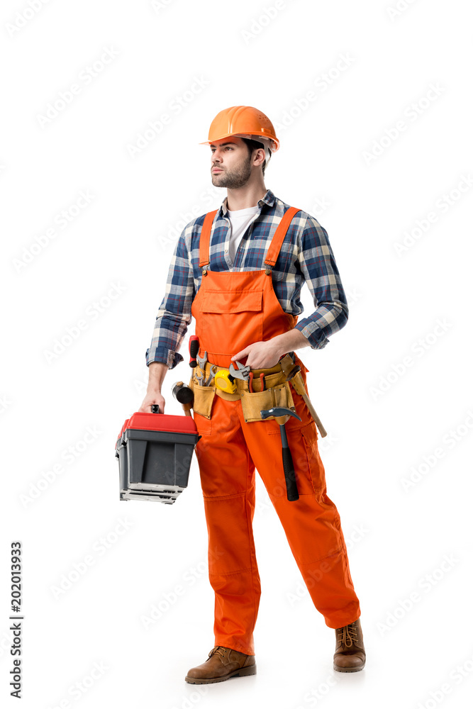 Young confident repairman in orange overall holding tool box isolated on white Young confident repairman in orange overall holding tool box isolated on white