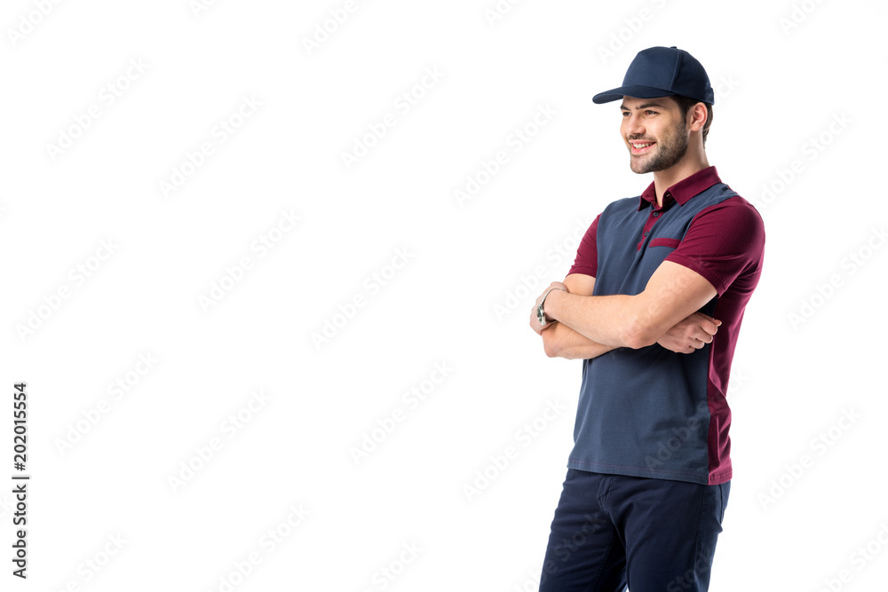 side view of smiling delivery man in cap with arms crossed isolated on white
