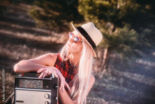 Portrait of an attractive young hipster girl sitting in a spring Park on a chair in the sun and holding a radio.
