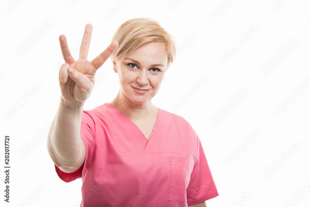 Attractive female nurse wearing pink scrubs showing number three Attractive female nurse wearing pink scrubs showing number three