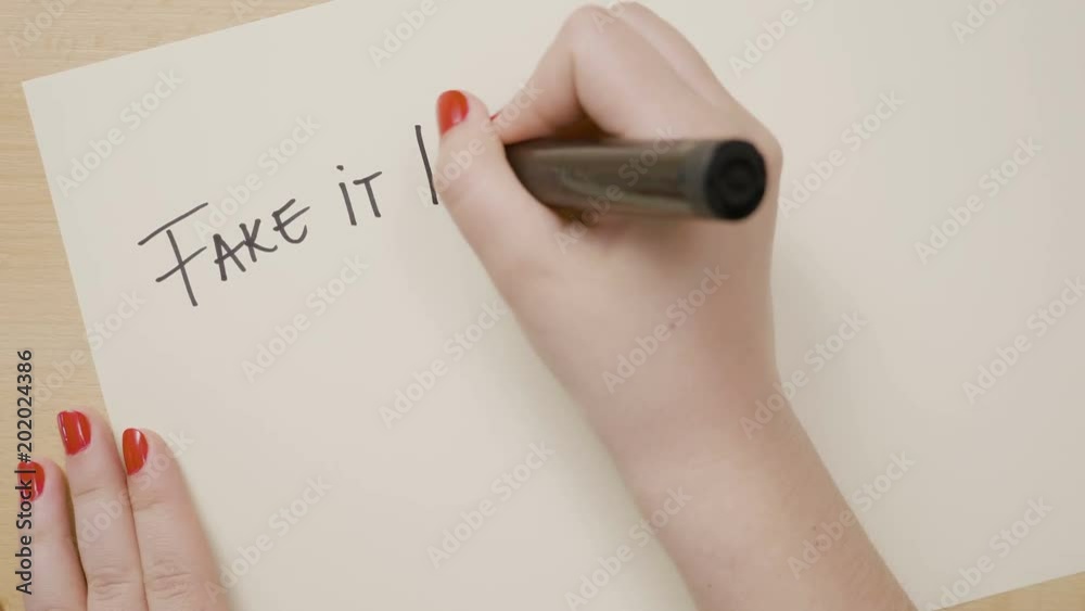 Woman hands writing fake it till you make it motivational quote on a white paper with black marker Woman hands writing fake it till you make it motivational quote on a white paper with black marker
