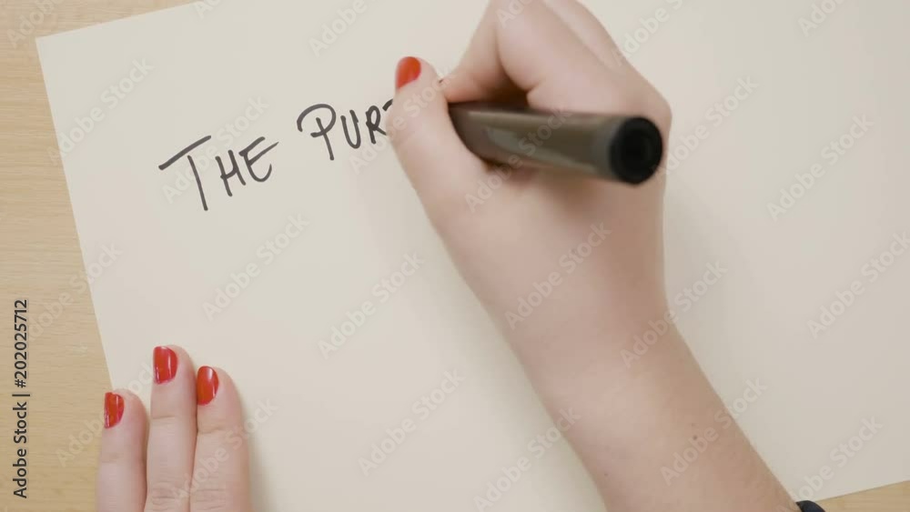 Female hands writing the purpose of our lives is to be happy motivational quote and drawing a smiley face on a white paper with a black marker Female hands writing the purpose of our lives is to be happy motivational quote and drawing a smiley face on a white paper with a black marker