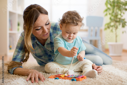 Baby toddler boy and mom playing in white sunny bedroom. Kids with educational toy in nursery.