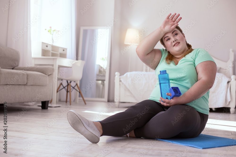 Workout rest. Plump young woman resting after workout while drinking her water Workout rest. Plump young woman resting after workout while drinking her water