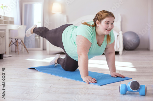 Basic exercises. Red-head young woman standing on the yoga mat while doing exercise