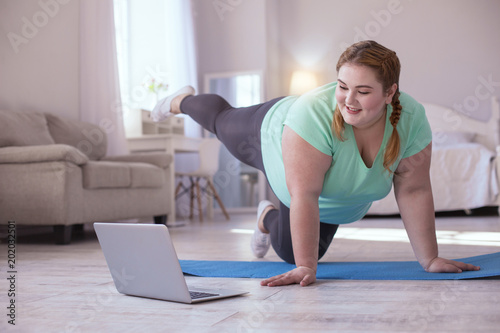 Video lesson. Obese young woman repeating exercises while watching online workout session