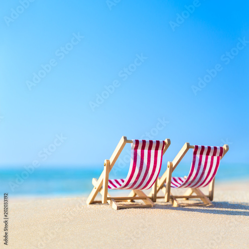Two striped red-white sunbeds at sandy tropical ocean beach in hot sunny day.