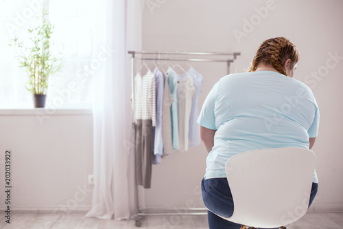 Clothing rack. Stout young woman feeling disappointed in herself while looking on the clothing rack