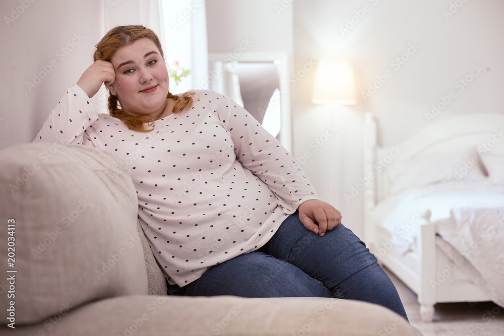 Future plans. Peaceful red-head woman sitting on the sofa while thinking about future Future plans. Peaceful red-head woman sitting on the sofa while thinking about future