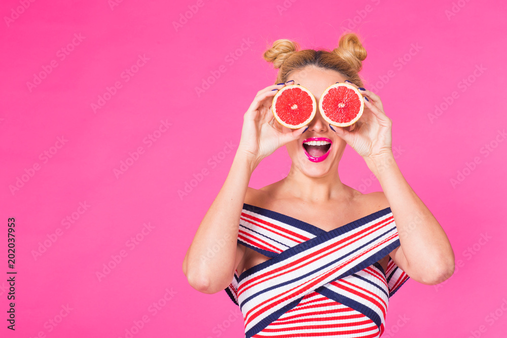 Beauty Model Girl takes Juicy Grapefruit. Beautiful Joyful young girl, funny blonde hairstyle and pink makeup.Holding Orange Slices and laughing, emotions.