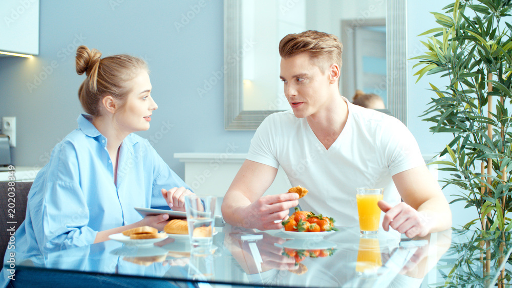Young couple using digital tablet while having breakfast at kitchen table. Young couple using digital tablet while having breakfast at kitchen table.