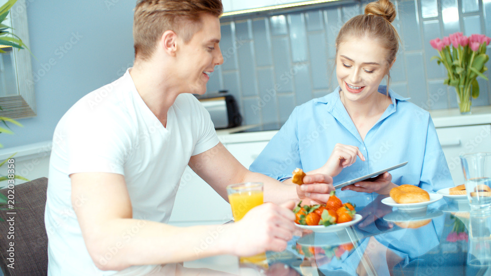 Young couple using digital tablet while having breakfast at kitchen table.