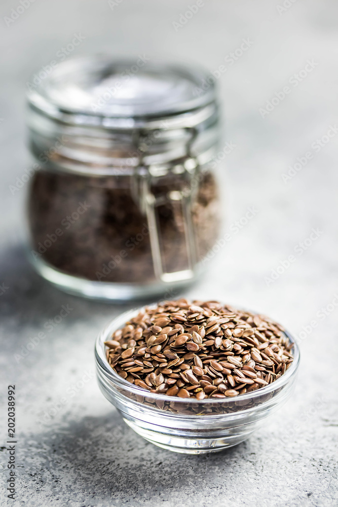 Flax seeds in glass jar and bowl on concrete background. Selective focus, space for text. Flax seeds in glass jar and bowl on concrete background. Selective focus, space for text.