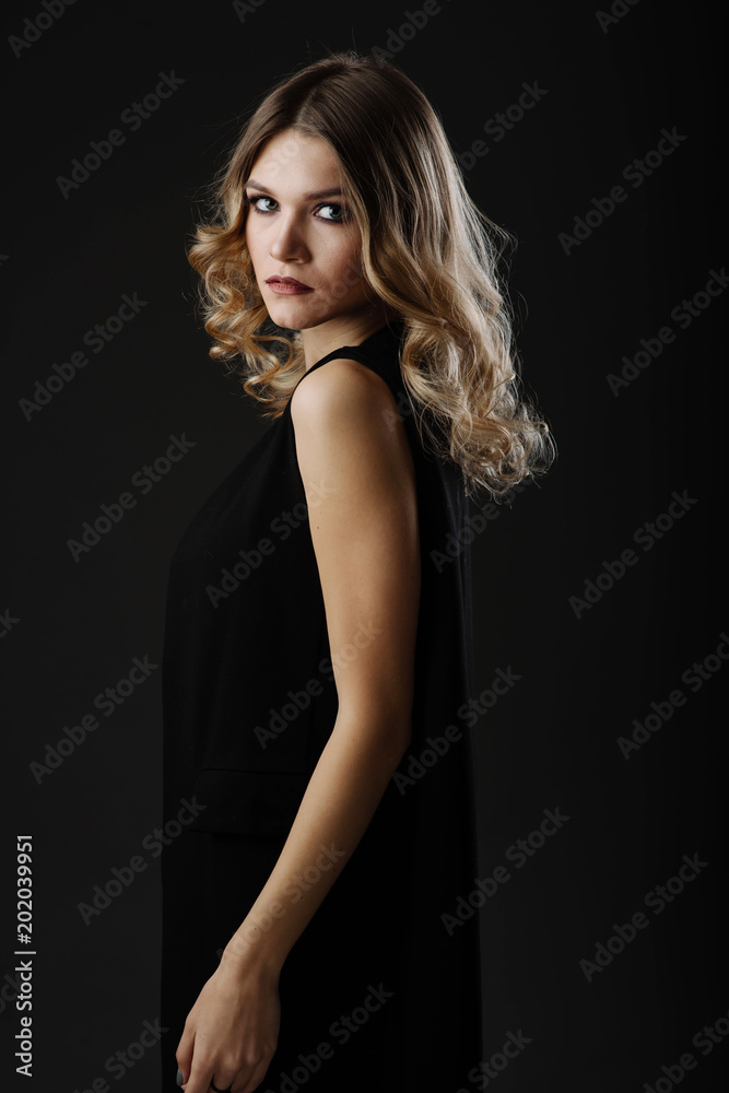 Beautiful blonde hair woman in black dress looking back while posing in the studio on black background. Fashion portrait