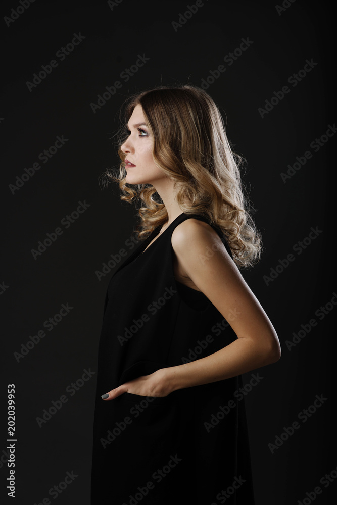 Side portrait of attractive blonde woman with curly hair, beautiful make up and black dress isolated on black background. Profile look Side portrait of attractive blonde woman with curly hair, beautiful make up and black dress isolated on black background. Profile look
