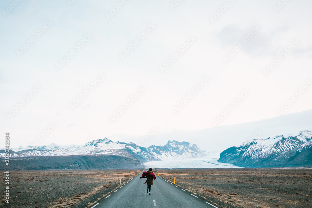 Woman running away to the road on a background of beautiful mountains. Iceland nature.