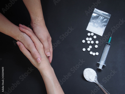 фотографія Holding hands for helping drug addict teenage on black table with drug powder, syringe and pills