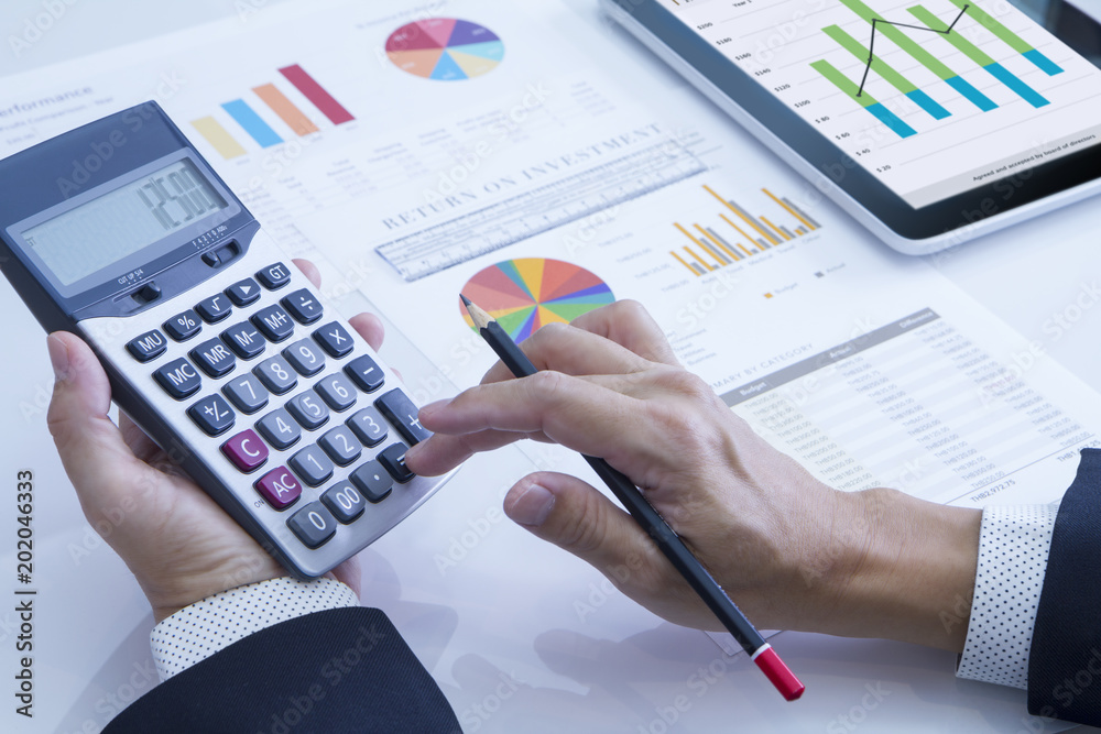 Businessman using calculator reviewing a financial report for a return on investment or investment risk analysis. Businessman using calculator reviewing a financial report for a return on investment or investment risk analysis.
