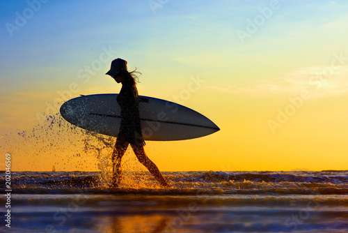 Принти на полотні Silhouette of woman holding surfboard beside walking on the edge of sea wave, sp