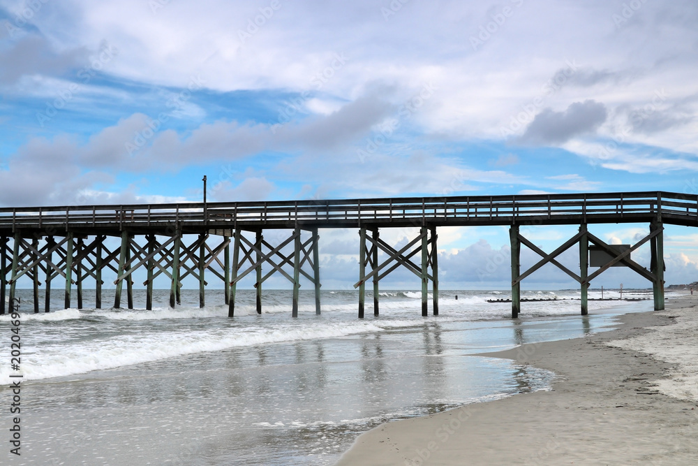Cloudy evening at Atlantic ocean beach. Atlantic ocean waves, scenic view with the wooden pier at Pawleys Island, South Carolina, Myrtle Beach area, USA.
