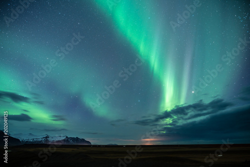 Northern light aka Aurora Borealis glowing on sky in Jokulsarlon glacier lagoon with snow capped mountains in background at night in Iceland © Jamo Images