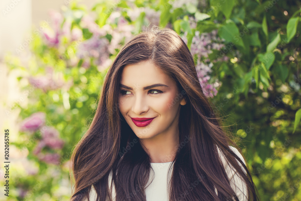 Spring woman outdoor. Cheerful smiling female model girl with healthy brunette hair in blossom park outdoors, cute face closeup Spring woman outdoor. Cheerful smiling female model girl with healthy brunette hair in blossom park outdoors, cute face closeup