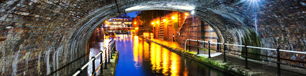 Tunnel in the city center during the rain, illuminated buildings at night, famous Birmingham canal in UK