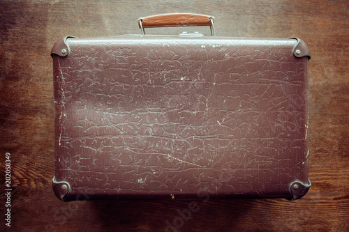 Old fashioned and shabby suitcase on the brown wooden background. Historical atmosphere. Retro things concept. Vintage style. photo